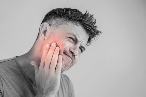  a man experiencing wisdom teeth pain holds his cheek